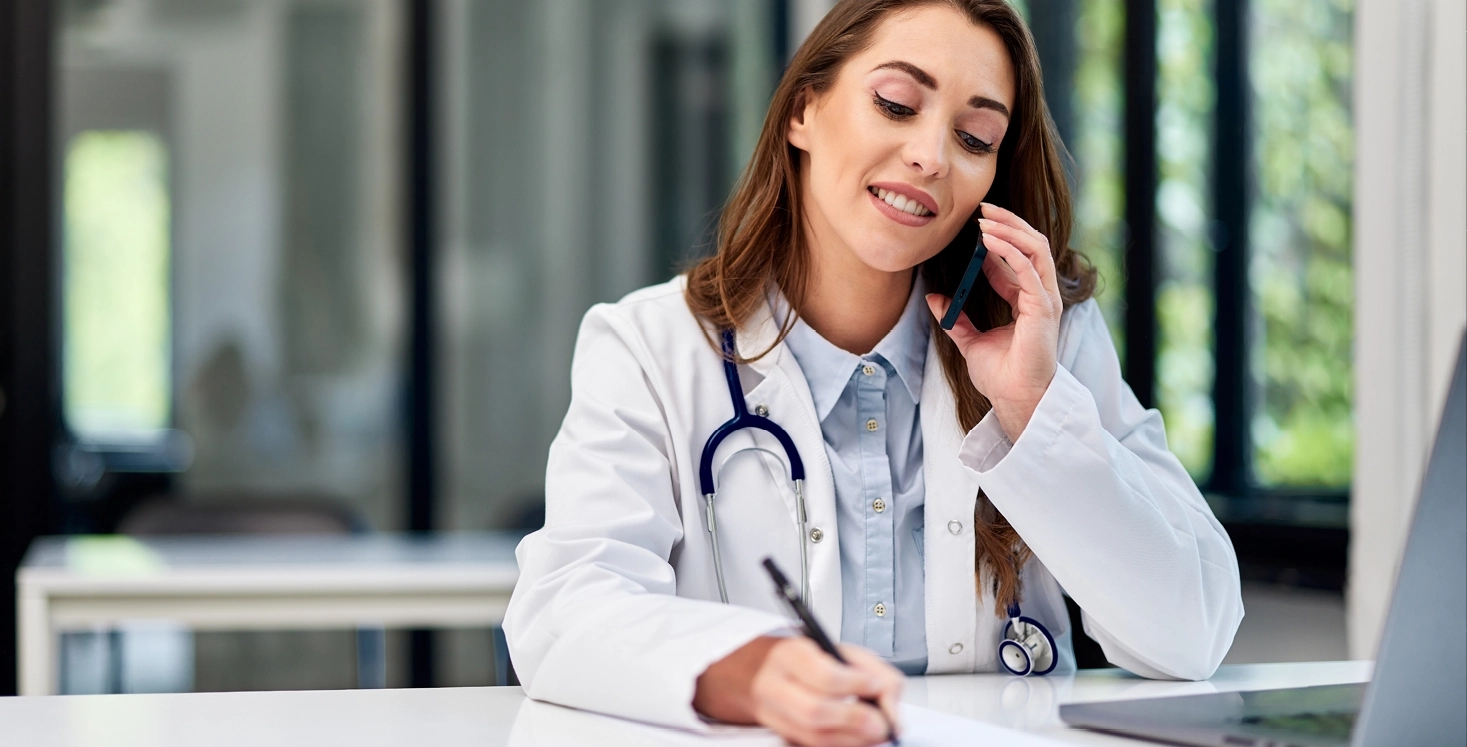 Arts die achter haar laptop zit en belt en iets opschrijft