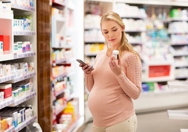 Zwangere in apotheek met potje medicijnen in haar hand.