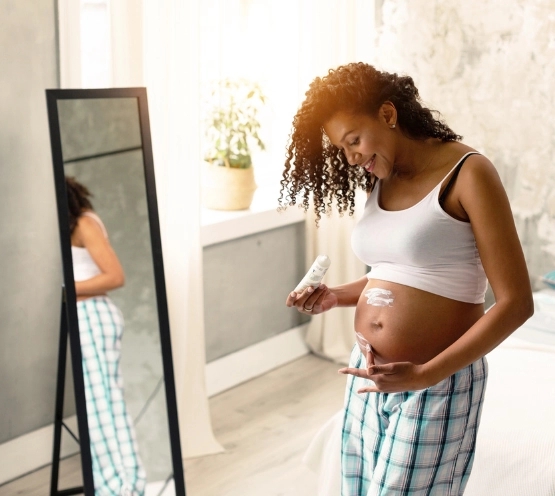 Een zwangere die crème smeert op haar buik voor de spiegel